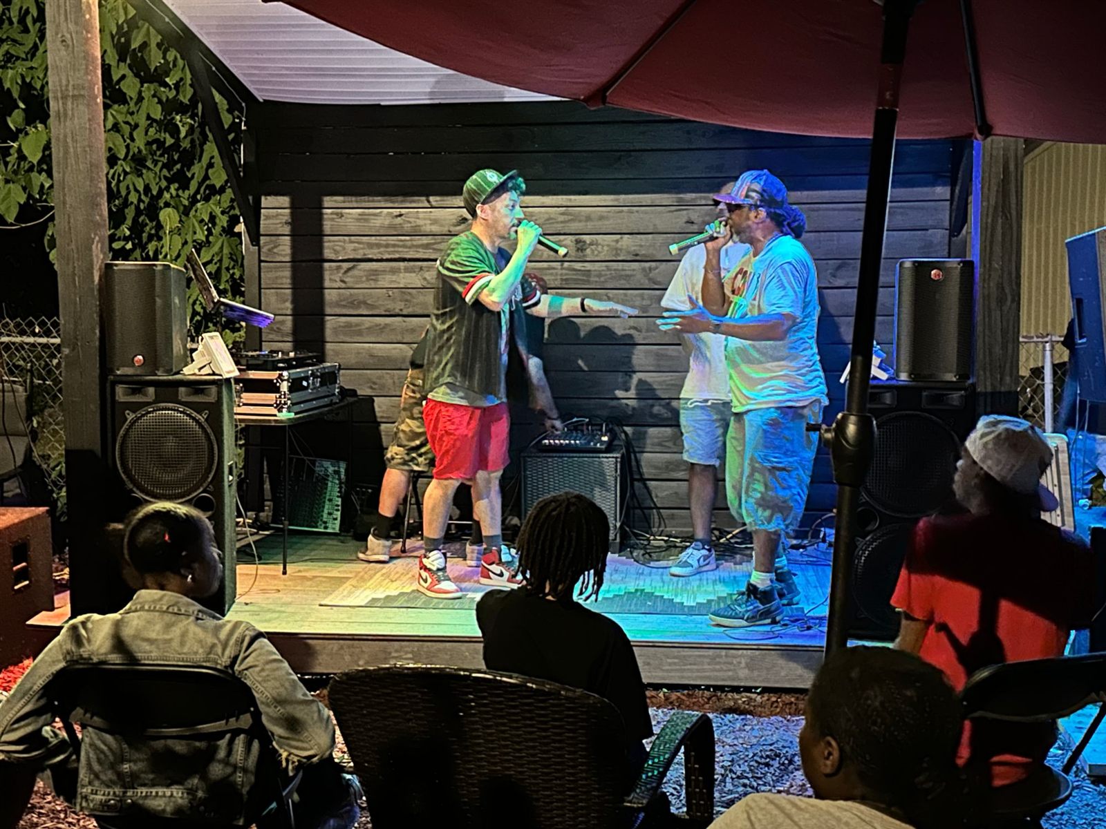 Two MCs trade rhymes on a small backyard stage at night