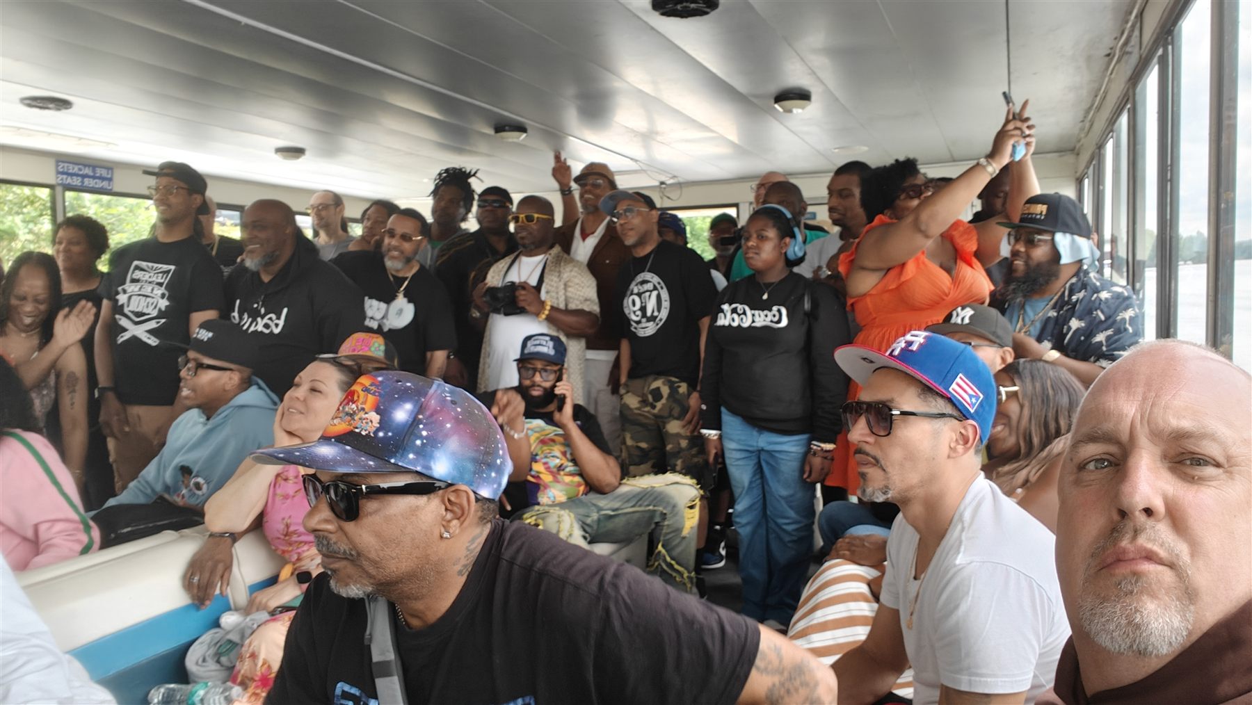 A packed boat cabin of Beats & Bars guests, many in black T-shirts, with hands raised toward the camera.