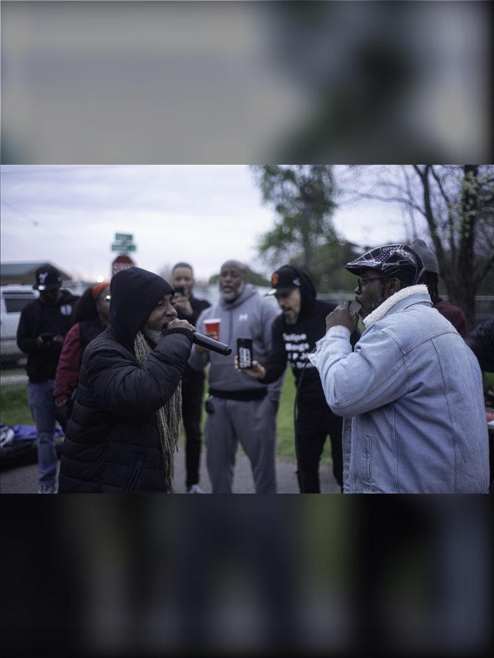 Two MCs on the mic with friends gathered around them, 2023.