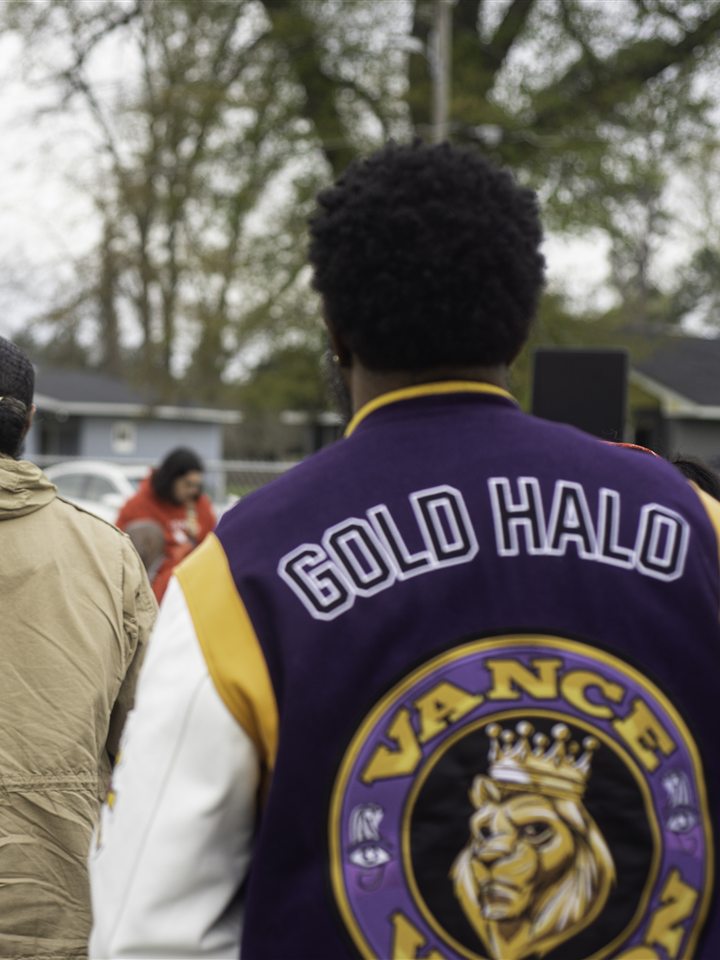 An audience member in a purple Gold Halo varsity jacket watches the show, 2023.