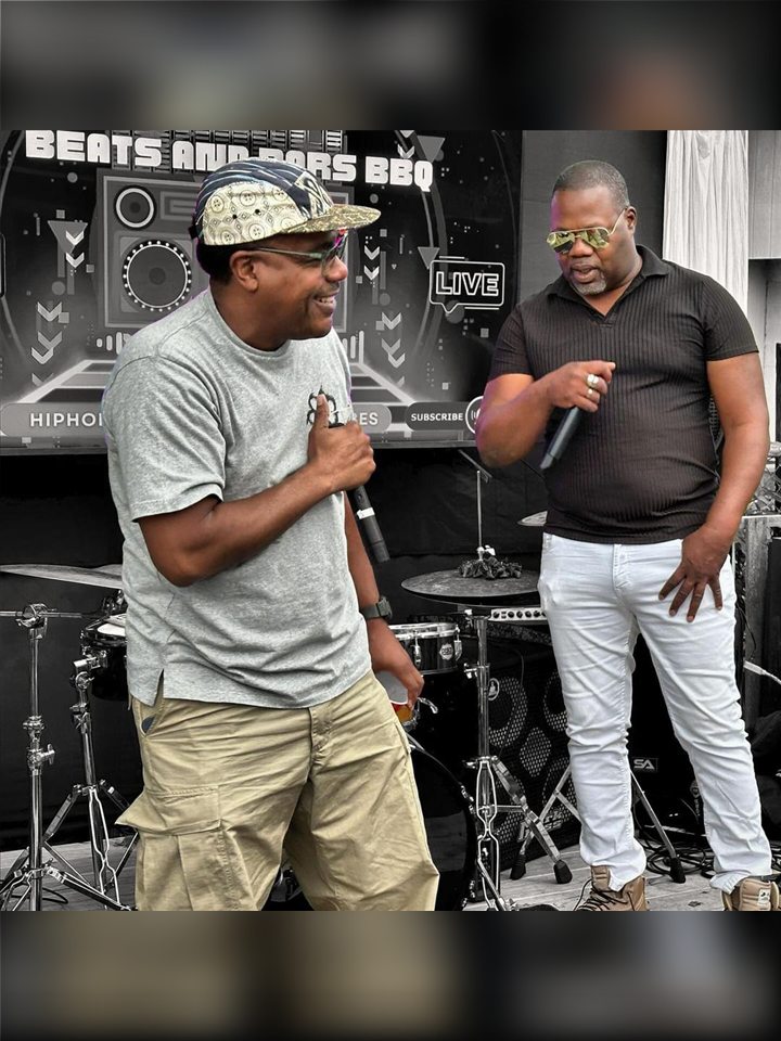 Two MCs on stage in front of the Beats & Bars BBQ backdrop, 2024.