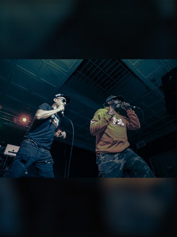 Two MCs on stage in the dark, 2025.